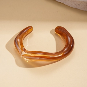 Close-up of translucent amber resin twisted cuff bangle on a beige aesthetic background