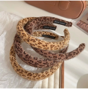 Detail of plush leopard print headbands with handmade tags on a soft fabric background