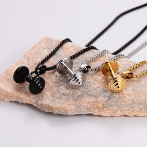 Three-color dumbbell pendants in black, silver, and gold on a stone base for fitness enthusiasts