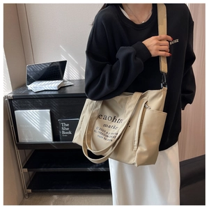 Detail of beige nylon tote bag with wide strap and side pocket worn by a model