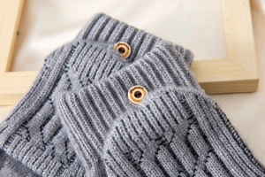 Detail of grey cable-knit fabric featuring a rustic wooden button with fashion engraving