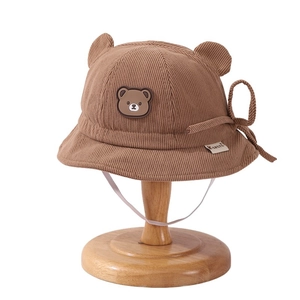 Brown corduroy baby bucket hat with cute bear ears and straps on a wooden stand