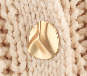 Close-up of matte gold irregular wave button on a thick chunky knit cardigan sweater