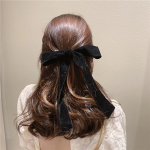 Detail of a large black velvet bow hair clip with long ribbons on wavy brown hair