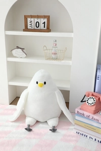 Soft white pigeon plush toy with yellow beak on a cozy pink checkered rug setting