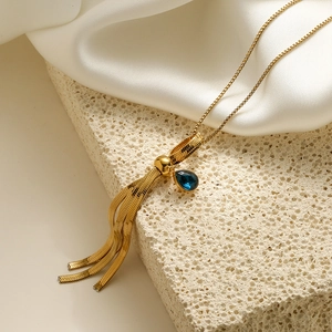 Gold plated tassel necklace with blue teardrop zircon on beige stone and silk background