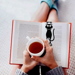 Close-up of black 3D cat bookmark shown in a cozy reading scene with a book and hot tea