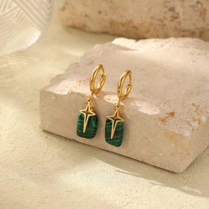Close-up of gold hoop earrings with green rectangular pendants and cross engraving