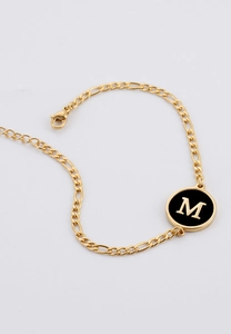 Detail of gold Figaro chain bracelet with a black enamel letter M charm and lobster clasp