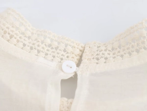 Macro shot of elegant lace collar detail with button closure on beige blouse