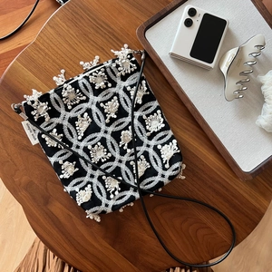 Crossbody canvas phone bag with white floral embroidery and tassel fringe on a wooden table