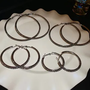 Exaggerated black rhinestone hoop earrings in four sizes on a white ceramic plate