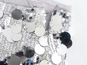 Detailed close-up of large silver sequins and mesh fabric with a hidden grey zipper