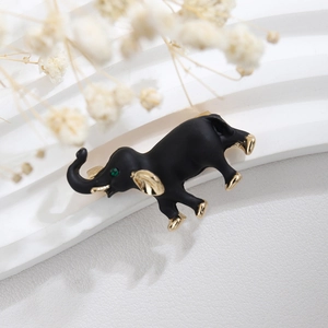 Modern matte black and gold elephant brooch with green gemstone eye on white pedestal