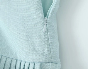 Detail shot of the side invisible zipper and pleated hem on light blue woven skirt