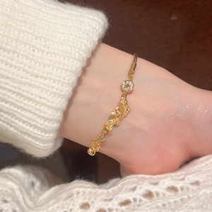 Detail of gold dragon charm bracelet with red zircons on model's wrist