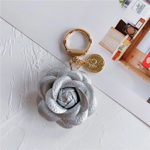 Detailed close-up of a silver leather camellia keychain with a golden coin charm