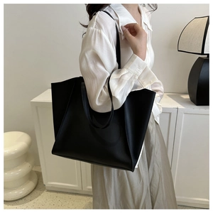 Minimalist black leather tote bag worn by a model in a clean, modern interior setting