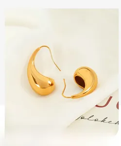 Macro view of 18K gold plated teardrop earrings on white fabric showing polished finish
