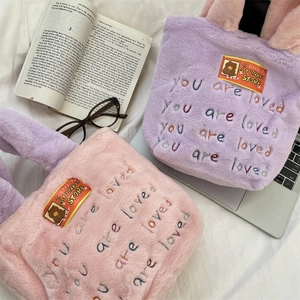 Vue à plat de sacs fourre-tout en peluche rose et violet avec broderie sur fond blanc texturé