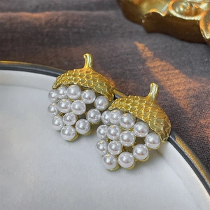 Close-up of vintage gold acorn earrings with white pearls on a ceramic plate