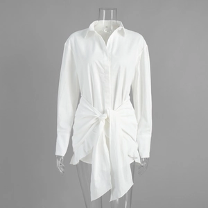 Detail of white long-sleeved shirt dress featuring waist knot design and textured fabric