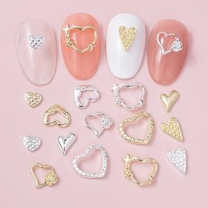 Close-up of heart nail art charms with rhinestones and floral details on pink background