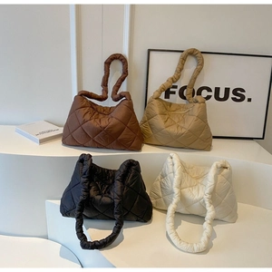 Multiple quilted puffy tote bags in brown, khaki, black, and white on a minimalist stand