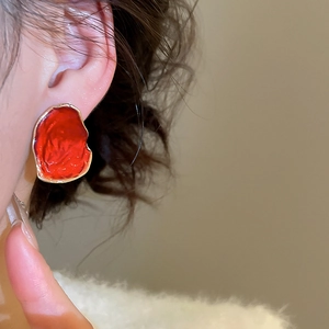 Nahaufnahme eines Models mit unregelmäßigen roten Emaille-Ohrsteckern mit Goldrand