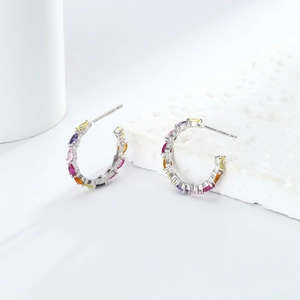 Detail of 925 silver C-shape earrings with colorful cubic zirconia on white stone