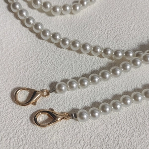 Close-up of white pearl bag chain with gold lobster clasp on textured white background