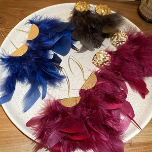 Detail of luxury feather tassel earrings in blue, burgundy, and brown with gold metal texture