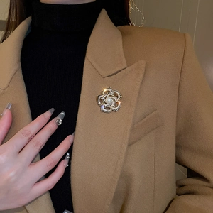 Détail de la broche camélia dorée avec perles et zircons sur une veste en laine