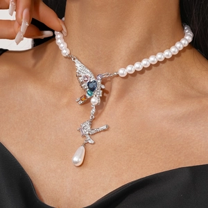 Detailed shot of pearl necklace with heart-shaped stone and bird pendant on a model