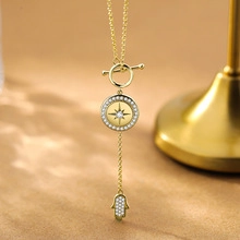 Detail of gold double chain necklace with Hamsa hand and starburst coin pendant with crystals