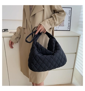 Close-up of black quilted nylon shoulder bag carried by a model in a beige trench coat