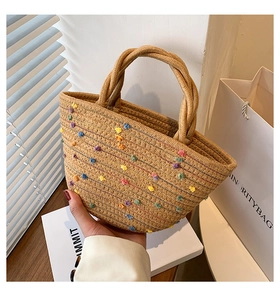 Detail of straw woven bucket bag with colorful pom-pom embroidery and rope handles