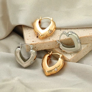 Detail of gold and silver heart-shaped hoop earrings with star zircons on silk