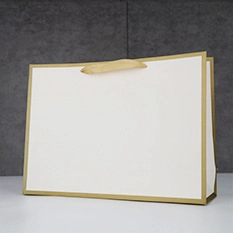 Close-up of white paper gift bag featuring gold foil trim and flat golden ribbon handles