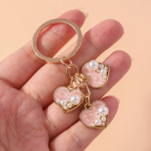 Golden keychain with pink heart pendants and pearls held against a peach background