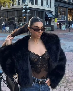 Détail d'une veste en fausse fourrure noire duveteuse avec body en dentelle et jean bleu