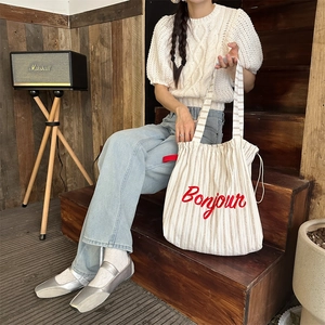 Detail of striped canvas tote bag featuring red Bonjour embroidery and fabric texture