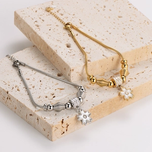 Gold and silver stainless steel snake chain bracelets with floral charms on travertine