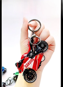 Handheld view showing a red mini motorcycle keychain with metal ring and spring clip