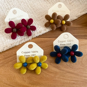 Macro detail of flocked flower stud earrings in burgundy, brown, yellow, and blue colors