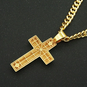 Gros plan d'un pendentif croix dorée avec motif de grille évidée sur une chaîne cubaine