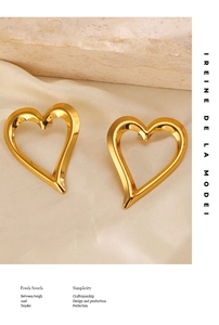 Detailed close-up of golden hollow heart earrings on elegant silk and stone background