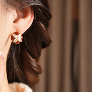 Close-up of a red flower earring with diamond center on a model's ear with silk background