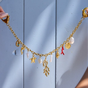 Detail of gold ocean-themed bag charm featuring shell, turtle, and dolphin pendants