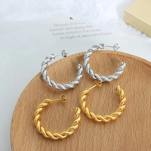 Retro twisted rope style C-shaped gold and silver earrings on a wooden display tray